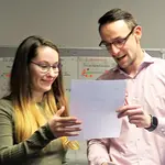 Zwei junge Erwachsene halten ein Blatt Papier und unterhalten sich darüber.
