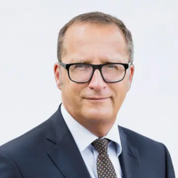 Herr Prexl trägt eine markante Brille und einen Anzug. 