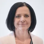 Frau Koehler trägt eine cremefarbene Jacke und schwarzes, kinnlanges Haar. Sie lächelt.
