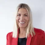 Constance von Struensee trägt einen roten Blazer, blondes schulterlanges Haar und lacht. 