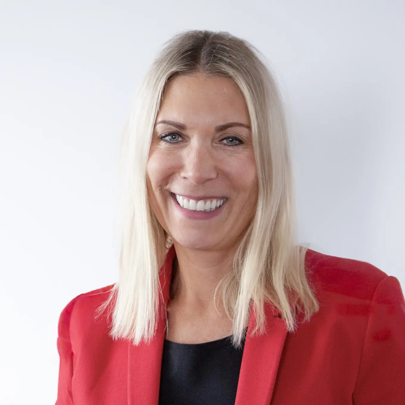 Constance von Struensee trägt einen roten Blazer, blondes schulterlanges Haar und lacht. 