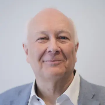 Dr. Ingo Habenicht befindet sich vor einem grauen Hintergrund und lächelt. 
