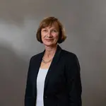 Martina Bender steht vor einem grauen Hintergrund und schaut mit seriösem Blick in die Kamera.