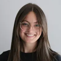 Frau Lara Kleineidam lacht, hat langes braunes Haar, trägt eine runde Brille und ein schwarzes Oberteil.
