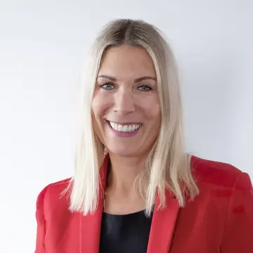 Constance von Struensee trägt einen roten Blazer, blondes schulterlanges Haar und lacht. 