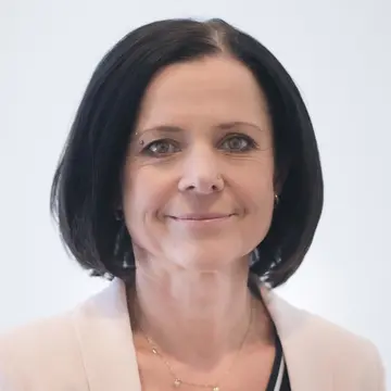 Frau Koehler trägt eine cremefarbene Jacke und schwarzes, kinnlanges Haar. Sie lächelt. 