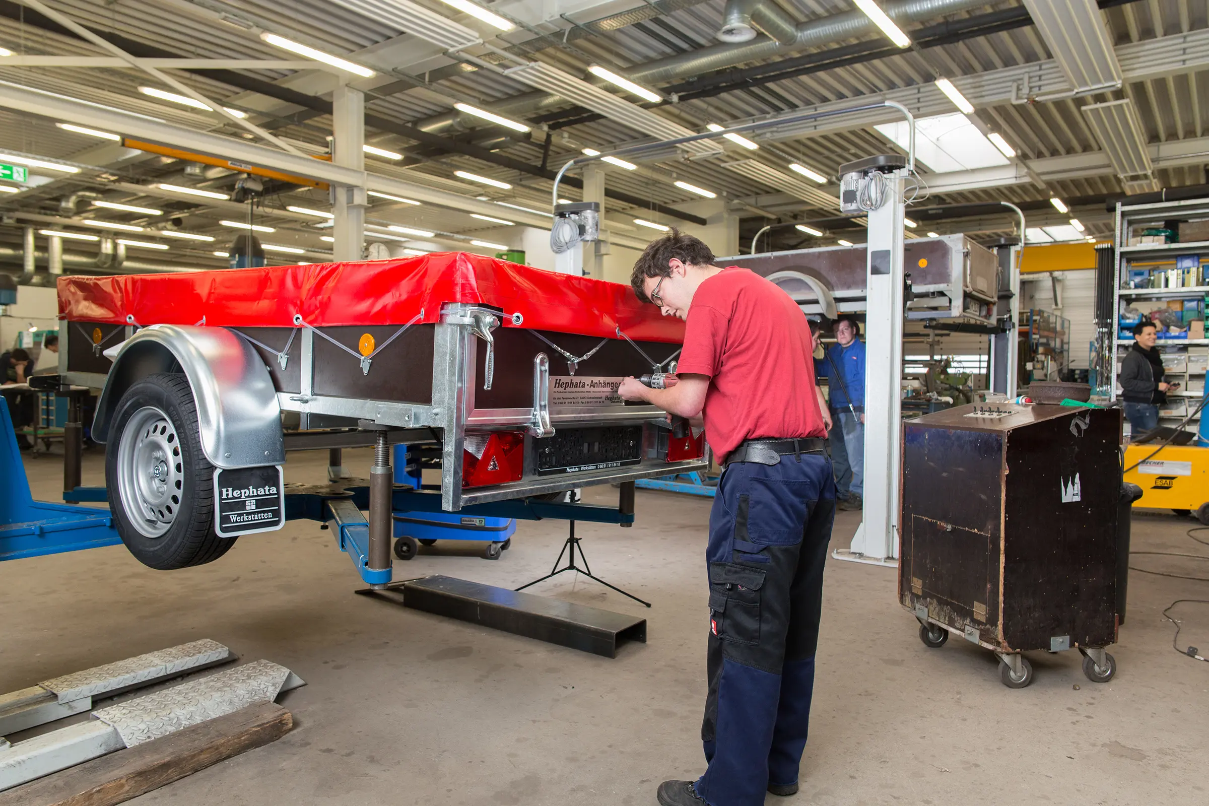 Ein Mitarbeiter steht in einer Fabrik und schraubt an einem Fahrgerät. 