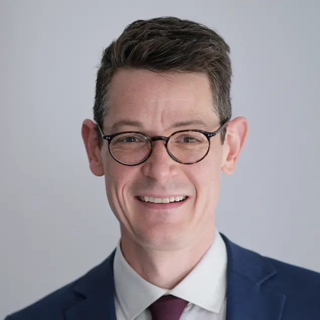 Dr. iur. Max Mälzer lacht. Er trägt Anzug, rote Krawatte und eine Brille. 