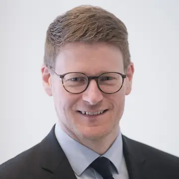 Herr Stark hat kurzes helles Haar und trägt eine Brille. Er lächelt und trägt einen Anzug. 