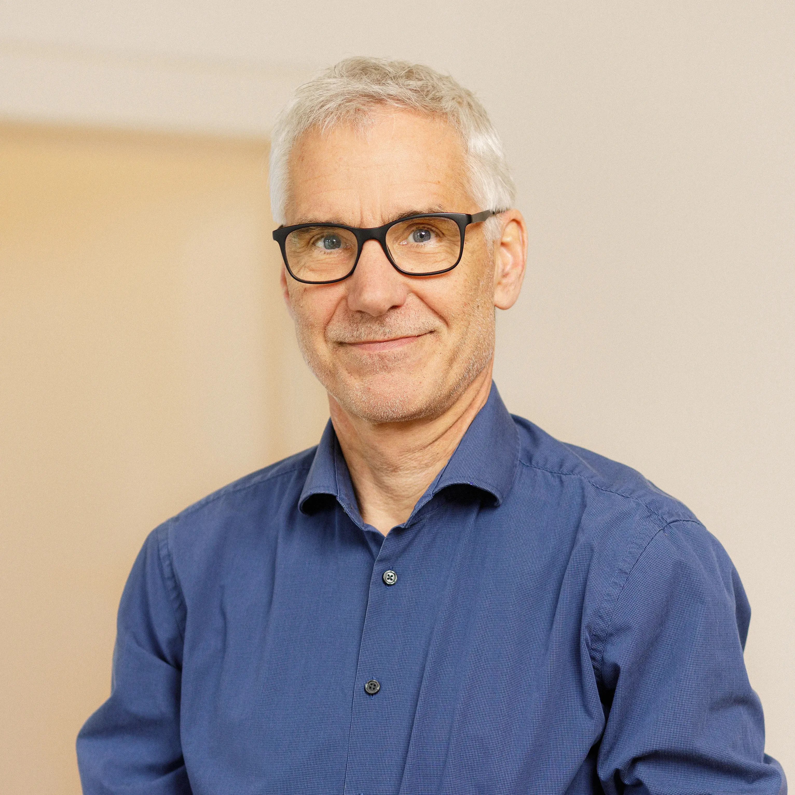 Herr Ragnitz trägt ein blaues Hemd und eine markante Brille. Er lächelt.