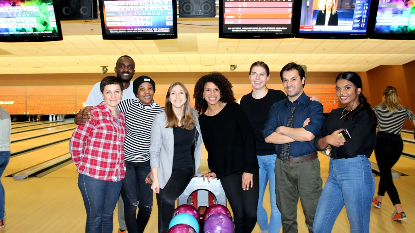 Acht junge Menschen stehen vor einer Bowlingbahn und lachen.