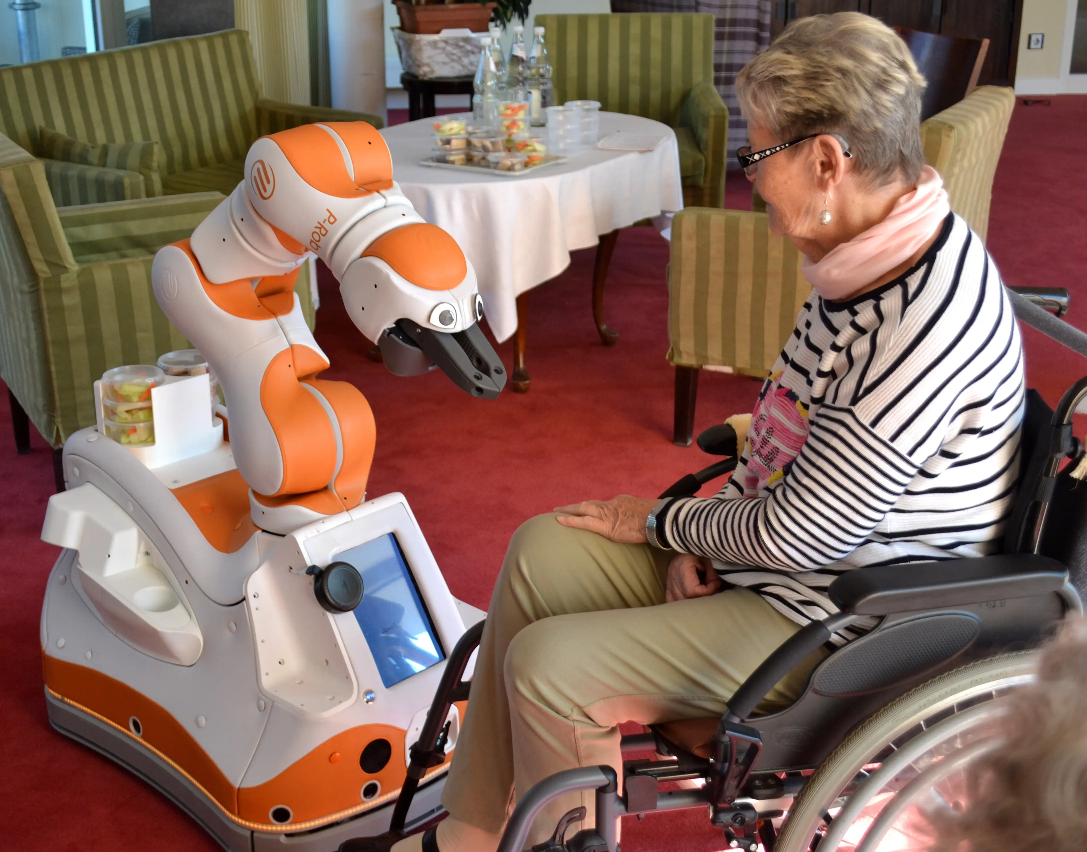 RoboterLIO und eine Frau im Rollstuhl sitzen sich gegenüber.