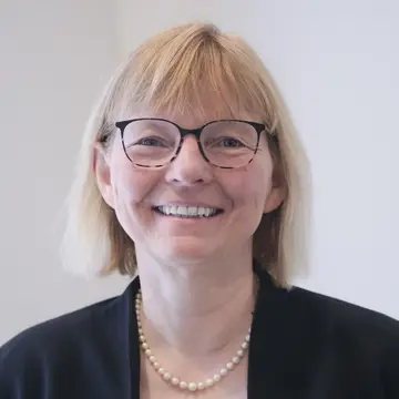 Frau Edda Weise trägt eine moderne Brille, eine schwarze Jacke und dazu eine helle Perlenkette. Sie lacht. 